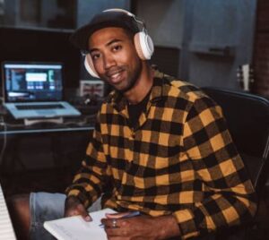 Man in yellow checkered shirt wearing headphones, smiling at camera.